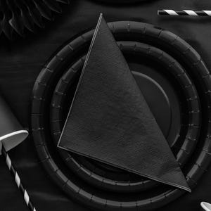Könnte beinhalten: Draufsicht auf eine schwarze Party-Tischdekoration. Enthält schwarze Pappteller, eine gefaltete schwarze Serviette, einen schwarzen Pappbecher und einen schwarz-weiß gestreiften Strohhalm. Die Teller haben ein geriffeltes Design.