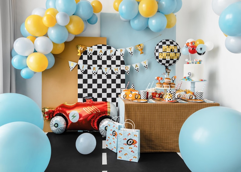 K&ouml;nnte beinhalten: Eine festliche Geburtstagsfeier mit Rennwagen-Motto. Enth&auml;lt einen roten Rennwagen-Ballon, karierte Dekorationen, einen Kuchen, Cupcakes und blaue, gelbe und wei&szlig;e Ballons. Die Worte "Happy Birthday" sind sichtbar.
