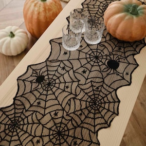 May include: Black and brown lace table runner with a spiderweb design. The runner has a scalloped edge and features black spiders and stars.
