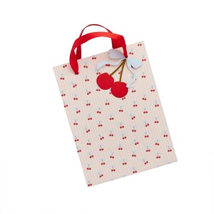 May include: A rectangular gift bag with a light pink and white vertical striped pattern featuring small red cherry illustrations. The bag has red ribbon handles and a decorative cutout of two red cherries with a light blue bow attached to the top.
