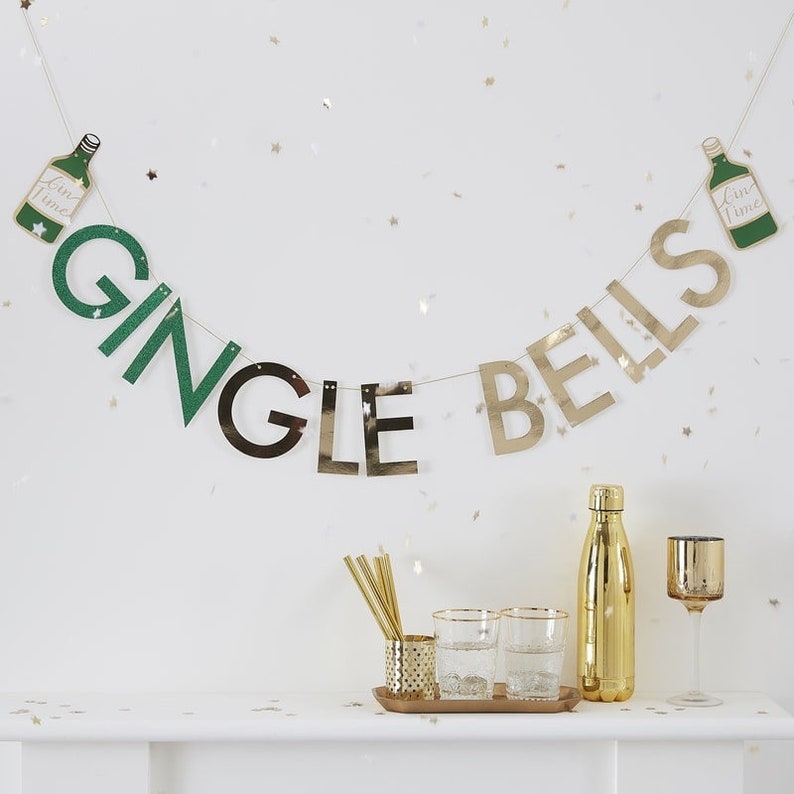 May include: A gold and green banner with the words "Gingle Bells" and two green bottles with the text "Gin Time" hanging on a white wall. The banner is decorated with gold glitter stars.