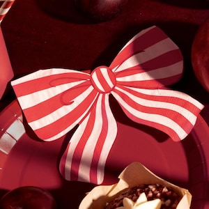 Könnte beinhalten: Eine rot-weiß gestreifte Papierservietten-Schleife auf einem roten Teller. Der Bogen ist der Mittelpunkt, mit einem kreisförmigen Zentrum und gebogenen Kanten. Der Hintergrund umfasst einen roten Teller, einen Cupcake und andere rote Gegenstände.