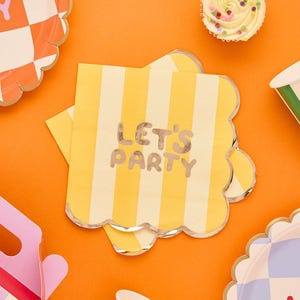 May include: A square yellow and white striped paper napkin with the text "LET'S PARTY" in silver lettering. The napkin has a scalloped edge with a silver border. Other party supplies are visible in the background.