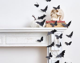 May include: A Halloween-themed display featuring black paper bats and butterflies, a white pumpkin, and a skull on a white mantelpiece. The bats and butterflies appear to be flying, creating a spooky, festive atmosphere.