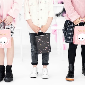 May include: Three children holding pink and black Halloween treat bags with a skeleton and bat design. The bags say "Boo!" on them.