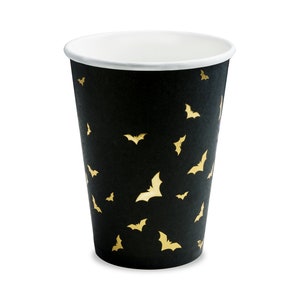 May include: A black paper cup with a white interior and a repeating pattern of gold-colored bats. The cup is designed for beverages and is suitable for Halloween or themed parties.