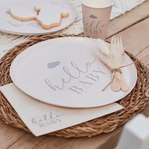 Può includere: Un set per baby shower rosa chiaro con le parole "hello BABY" in corsivo grigio. Il set include un piatto, un tovagliolo e una tazza, tutti con lo stesso design. Il piatto ha una grafica a nuvola. Il set è su un sottobicchiere intrecciato.