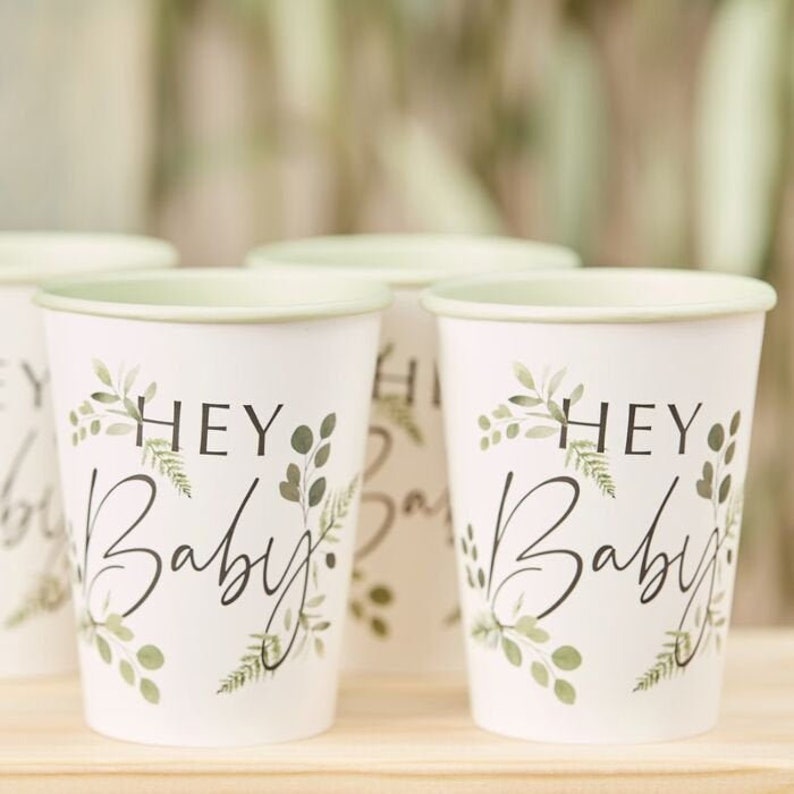 K&ouml;nnte beinhalten: Satz mit vier wei&szlig;en Pappbechern mit gr&uuml;nem Blattdesign und dem Text "Hey Baby" in Schwarz.