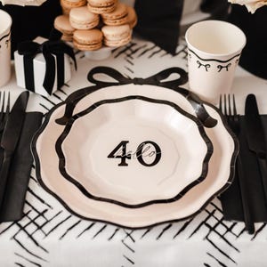 May include: A party table setting with a black and white theme. The centerpiece is a plate with the number "40" and the word "hello" printed on it. There are also black cutlery, a gift box, and a cup.