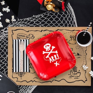 May include: A red paper plate featuring a pirate skull and crossbones design with the word "ARR!" on it. The plate is placed on a brown paper placemat with a treasure map design. There are also black and white striped napkins, a wooden fork, and a black pirate hat in the image.