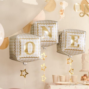May include: Three square foil balloons featuring a beige and white gingham pattern with a scalloped gold border. Each balloon displays a large, metallic gold letter, spelling out the word ONE. Gold star-shaped cutouts hang from each balloon.