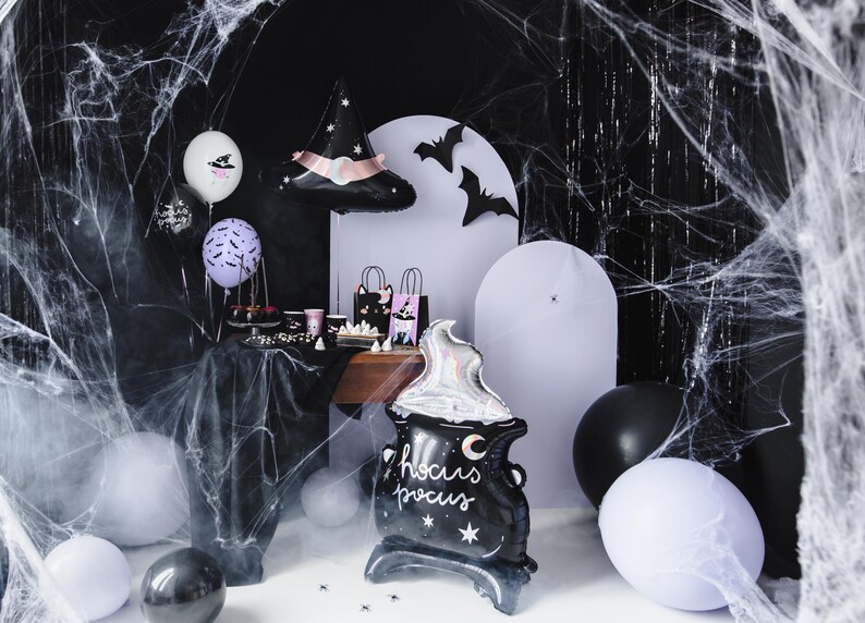 May include: A black cauldron balloon with the text "Hocus Pocus" and a crescent moon. The balloon is surrounded by white, black, and purple balloons, a witch hat balloon, and black bats. The background is a black and white spiderweb.