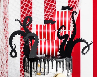 Puede incluir: Un pastel blanco y negro decorado con barcos piratas de papel a rayas rojas y blancas y siluetas de pulpos de papel negro.