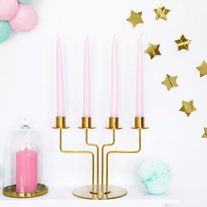 May include: A gold metal candelabra with four pink candles. The candelabra has a round base and three arms. The candles are in a glass cloche with a pink candle.