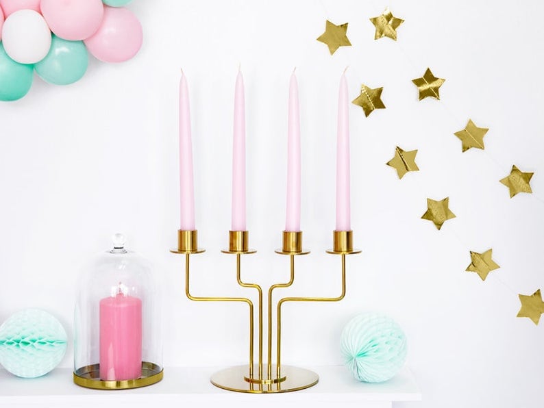 May include: A gold metal candelabra with four pink candles. The candelabra has a round base and three arms. The candles are in a glass cloche with a pink candle.