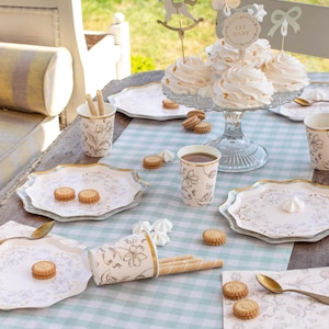 May include: A baby shower table setting with cupcakes, biscuits, and paper goods. The table is covered with a light blue and white checked tablecloth. The cupcakes are topped with decorative toppers that say "Oh Baby".