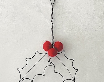 May include: A handcrafted Christmas ornament featuring a holly leaf design. The ornament has black wire leaves and three red felt berries. The total length is 13 cm (5.1 inches).