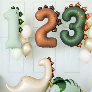 Puede incluir: Decoraciones de cumpleaños con temática de dinosaurios. Incluye globos inflables con los números 1, 2 y 3 en verde, bronce y verde oscuro. También presenta dos figuras inflables de dinosaurios.