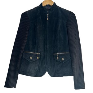 May include: Black suede jacket with ribbed knit sleeves. The jacket features a stand-up collar, a front zipper, and two front pockets with decorative zipper pulls. The jacket is hanging on a wooden hanger.