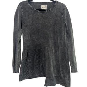 May include: A charcoal gray long-sleeve top with a unique asymmetrical design. The top features a crew neck and ribbed cuffs. The fabric has a textured, washed appearance. The top has a label that reads "M. Rena".