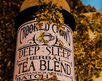 May include: A black jar with a cork lid filled with dried herbs. The label reads "Crooked Crows Deep Sleep Herbal Tea Blend Handcrafted Batch".