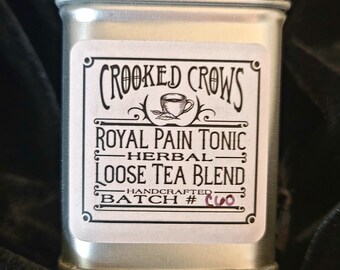 Pode incluir: Uma lata de prata com um rótulo branco que diz "CROOKED CROWS ROYAL PAIN TONIC HERBAL LOOSE TEA BLEND HANDCRAFTED BATCH #CUO". A lata mede 2,5 polegadas por 1,7 polegadas e contém uma onça de chá.