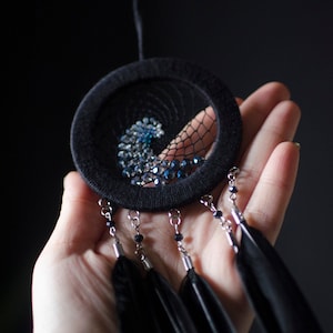 May include: A black dreamcatcher with blue and silver beads and black feathers hanging from it.