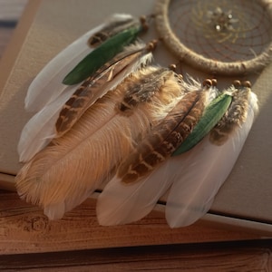 May include: A brown and white dream catcher with green feathers hanging from a brown box.