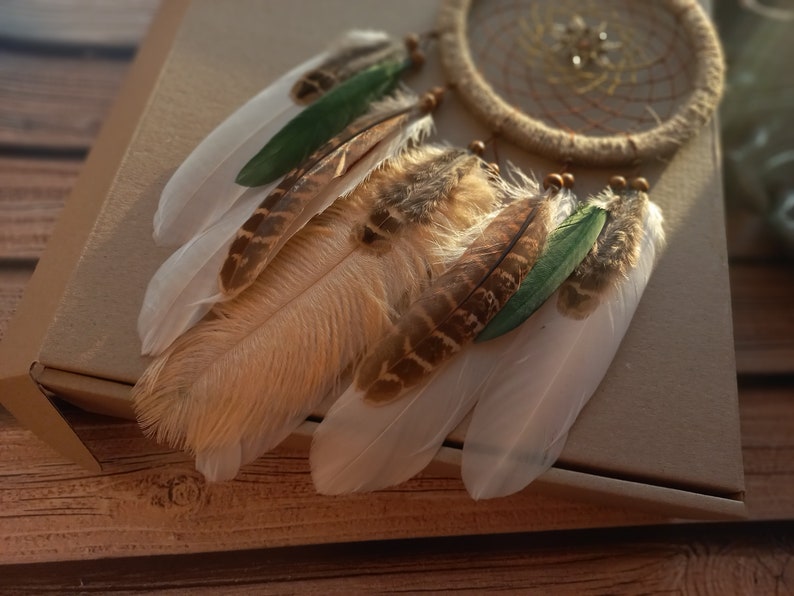 May include: A brown and white dream catcher with green feathers hanging from a brown box.