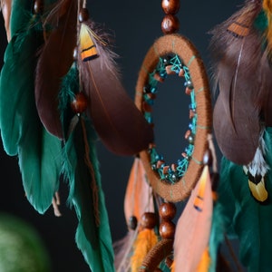 May include: A brown and teal dreamcatcher with feathers and wooden beads. The dreamcatcher has a circular frame with a web-like pattern and is decorated with beads and feathers.