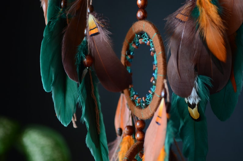 May include: A brown and teal dreamcatcher with feathers and wooden beads. The dreamcatcher has a circular frame with a web-like pattern and is decorated with beads and feathers.