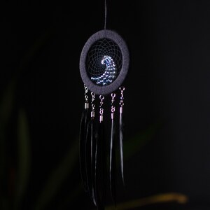 May include: A black dreamcatcher with a beaded design in the shape of a wave. The dreamcatcher has black feathers hanging from it.