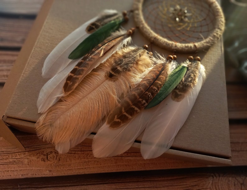 May include: A dream catcher with brown and white feathers, green accents, and a brown woven net.
