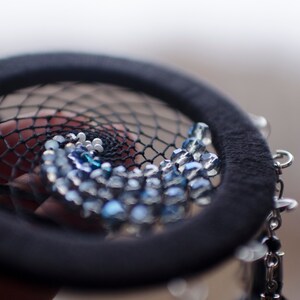 May include: A black dreamcatcher with a beaded design featuring blue and white beads. The beads are arranged in a spiral pattern.