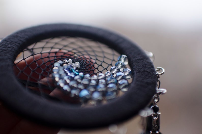 May include: A black dreamcatcher with a beaded design featuring blue and white beads. The beads are arranged in a spiral pattern.