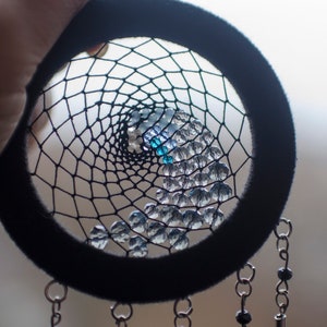 May include: A black dreamcatcher with a beaded web and blue and clear beads. The dreamcatcher has black feathers hanging from the bottom.