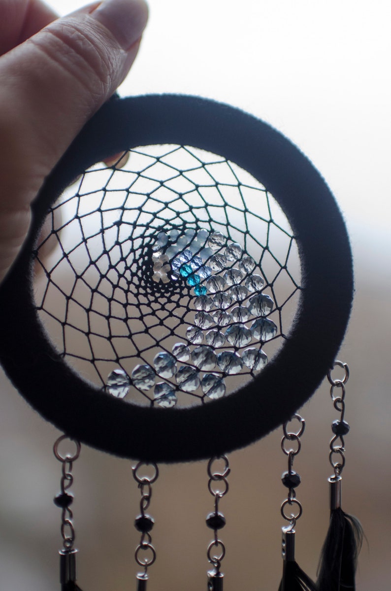 May include: A black dreamcatcher with a beaded web and blue and clear beads. The dreamcatcher has black feathers hanging from the bottom.