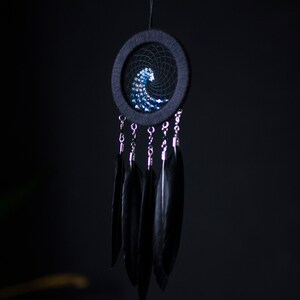 May include: A black dreamcatcher with a blue and white wave design and black feathers hanging from it.