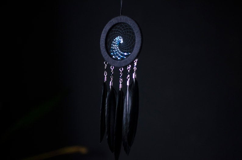 May include: A black dreamcatcher with a blue and white wave design and black feathers hanging from it.