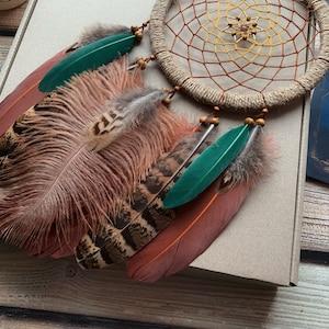 May include: A brown, green, and white dream catcher with feathers. The dream catcher has a beaded border and a woven web.