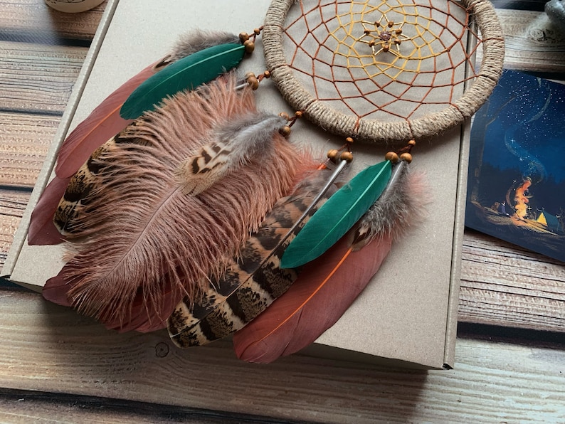 May include: A brown, green, and white dream catcher with feathers. The dream catcher has a beaded border and a woven web.
