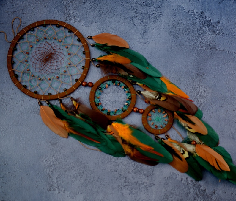 May include: A brown dreamcatcher with green, orange, and brown feathers. The dreamcatcher has a beaded outer ring and a smaller beaded ring in the center.