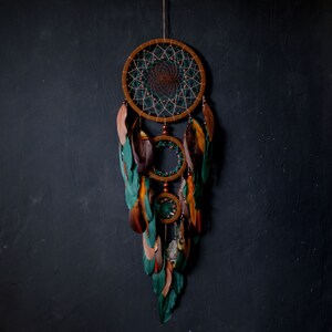 May include: A green, brown, and white dreamcatcher with feathers hanging from the bottom. The dreamcatcher is made of macrame and has a circular design.