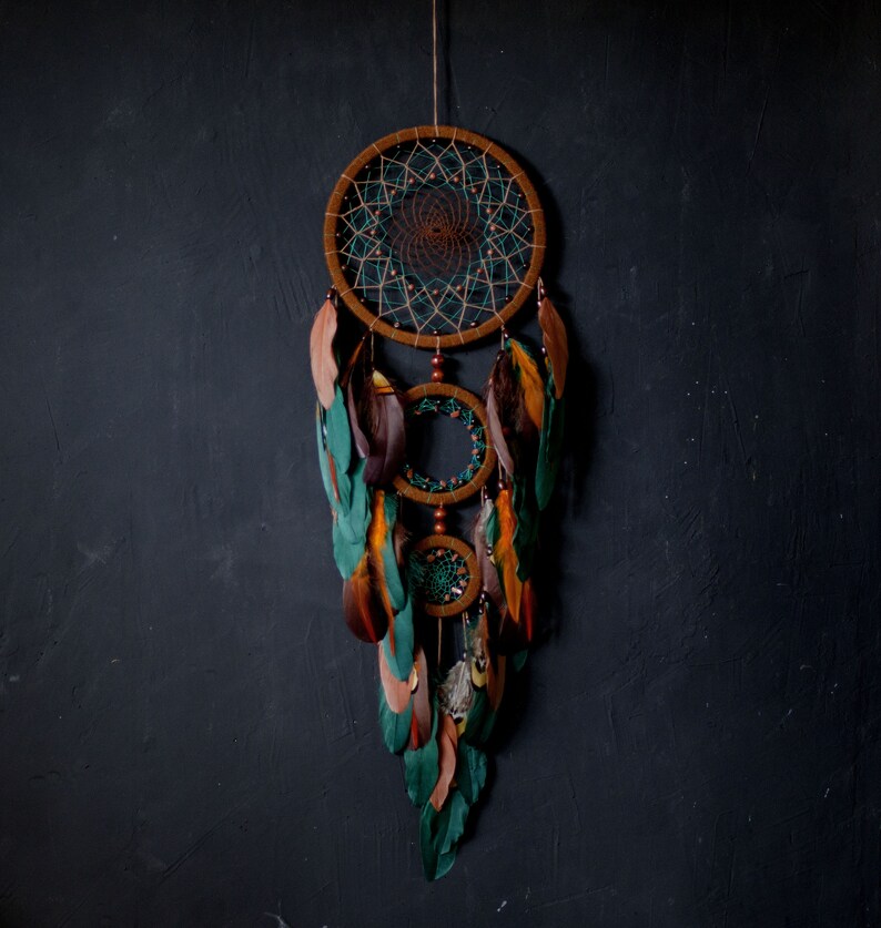May include: A green, brown, and white dreamcatcher with feathers hanging from the bottom. The dreamcatcher is made of macrame and has a circular design.