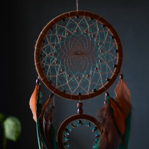May include: A brown dreamcatcher with teal and brown feathers hanging from it. The dreamcatcher has two hoops, one larger than the other, and is decorated with beads.