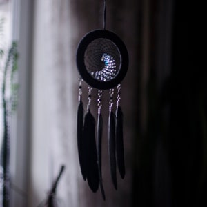 May include: A black dreamcatcher with a beaded web and black feathers hanging from it.