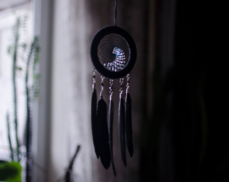 May include: A black dreamcatcher with a beaded web and black feathers hanging from it.
