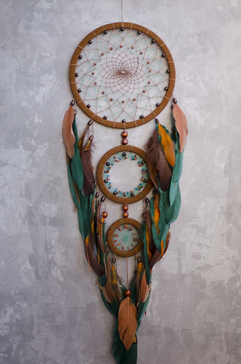 May include: A brown and green dreamcatcher with feathers and beads hanging from it. The dreamcatcher has three hoops, with the largest hoop at the top and the smallest hoop at the bottom.