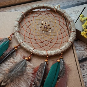 May include: A brown and beige dreamcatcher with a red and yellow net, beaded center, and brown feathers.
