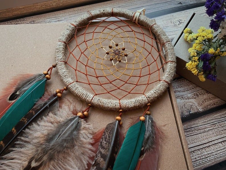 May include: A brown and beige dreamcatcher with a red and yellow net, beaded center, and brown feathers.